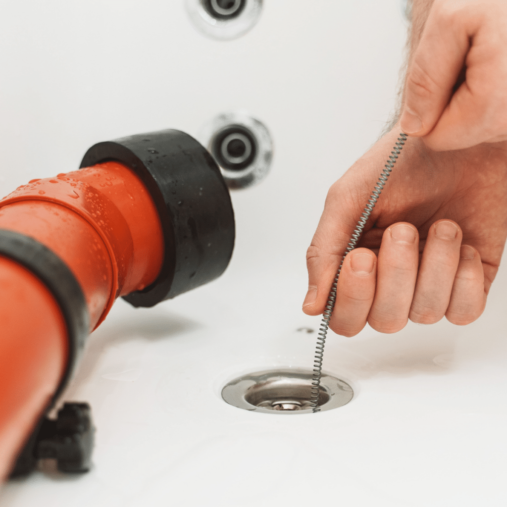 A hand using a plumbing snake to unclog a bathtub drain