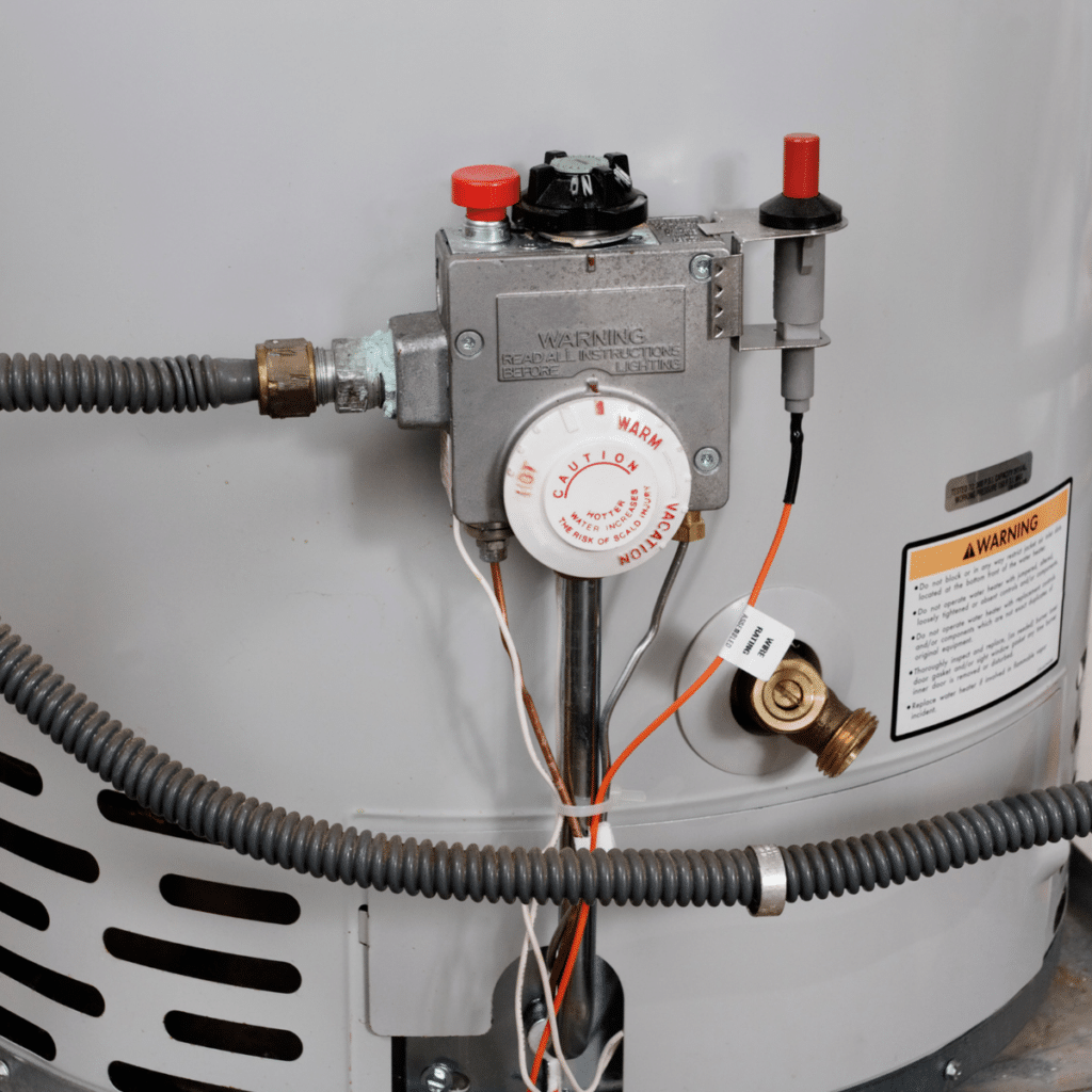 A close-up of a gas water heater’s thermostat and warning labels