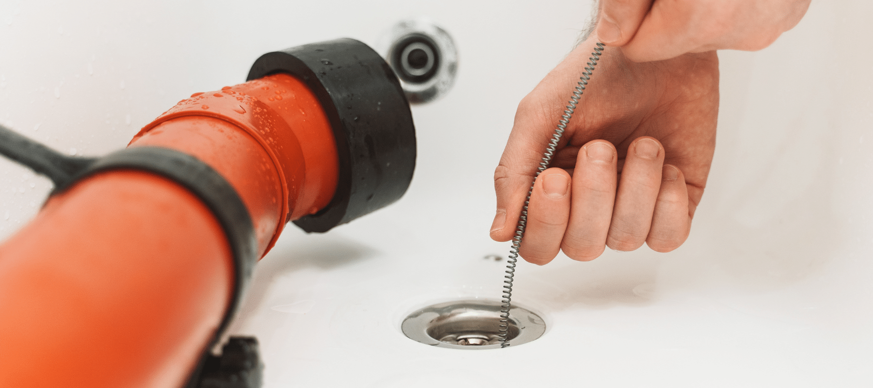 A hand using a plumbing snake to unclog a bathtub drain