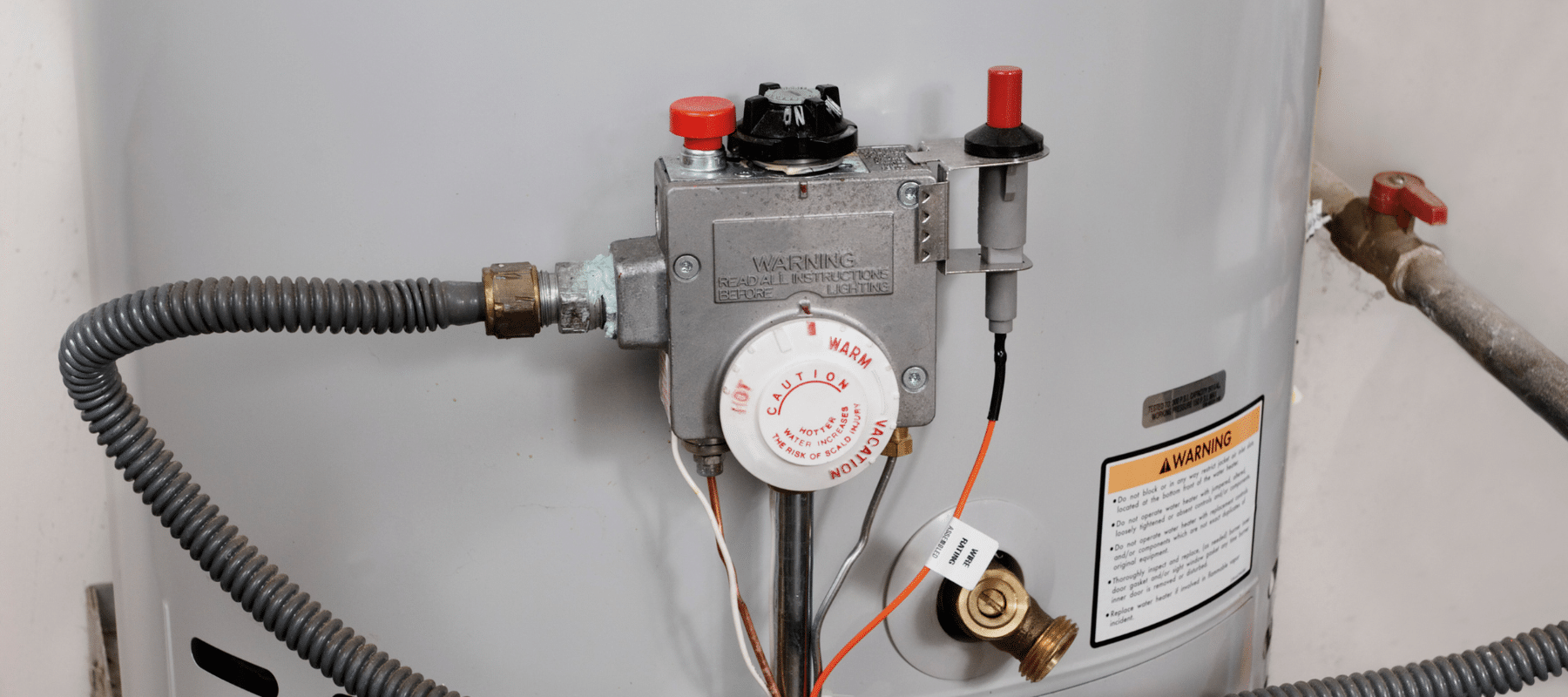 A close-up of a gas water heater’s thermostat and warning labels